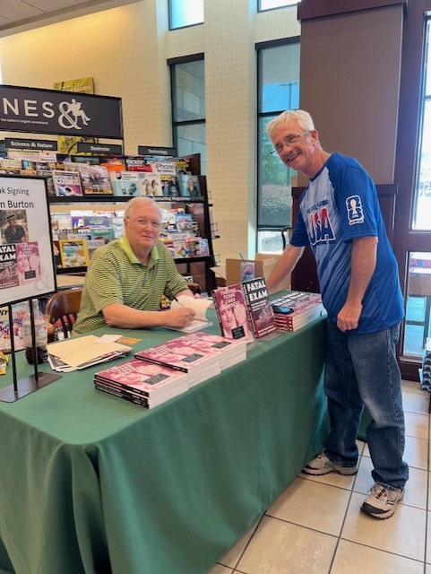 Alan Burton at a table signing books for visitors